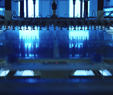 Close-up of industrial printer head with multiple nozzles printing on a large flat surface under blue lighting.