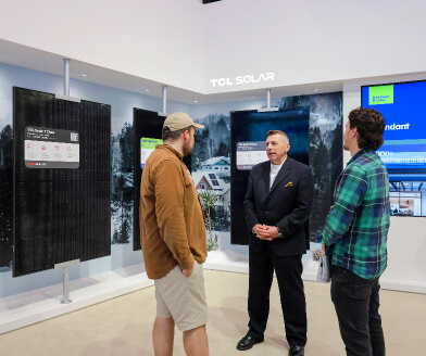 Three men engaged in conversation in front of TCL Solar display panels at an indoor exhibition.