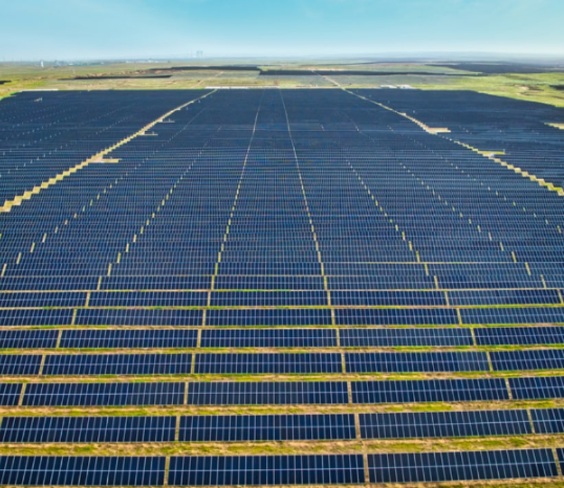 Aerial view of a large solar farm with rows of solar panels stretching across the landscape under a clear blue sky.