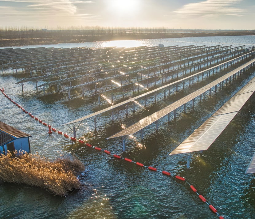 Rows of solar panels installed above water with sunlight reflecting on the surface during sunset.