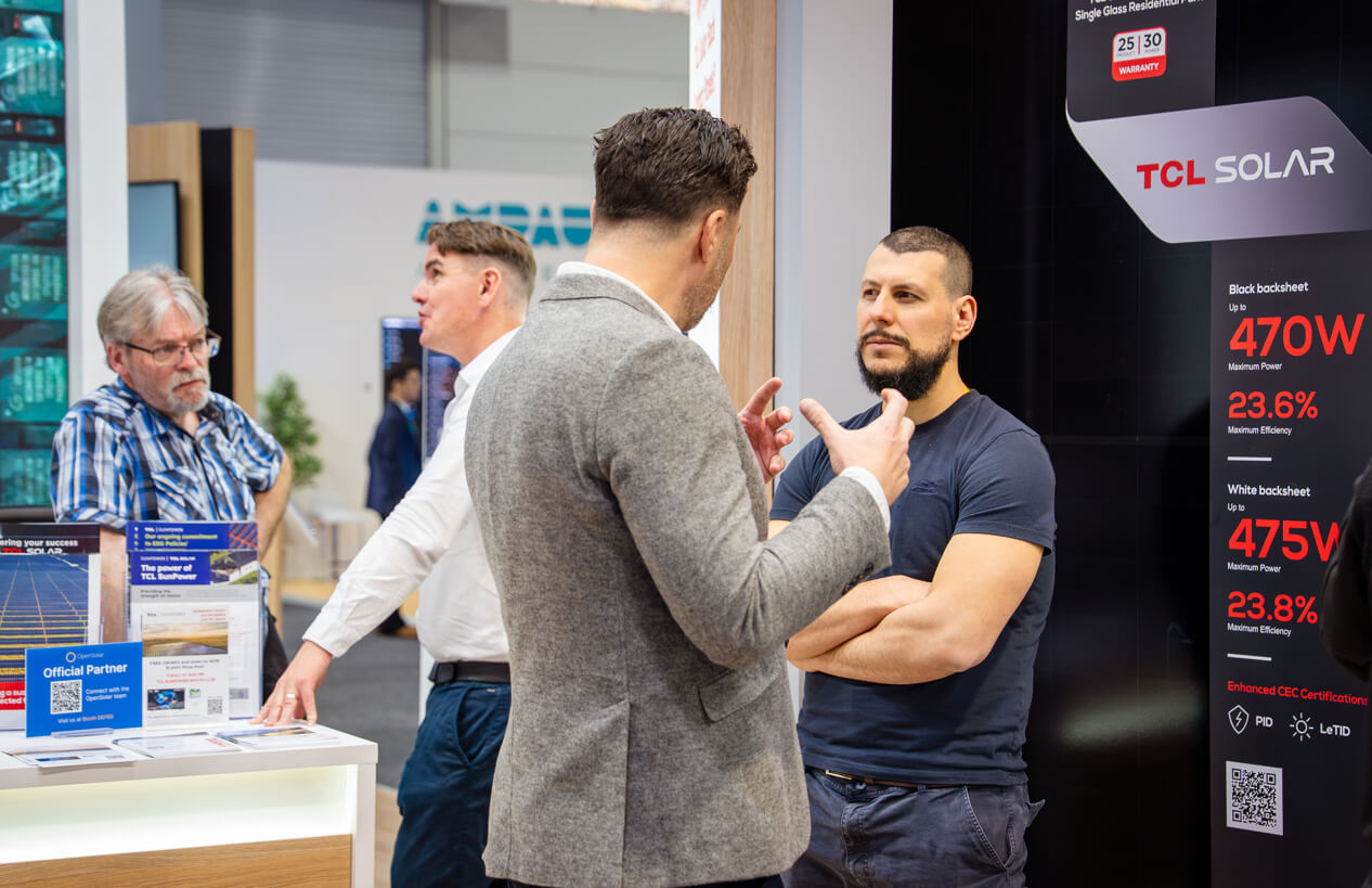 Four men engaged in discussion at a TCL Solar booth displaying solar panel power and efficiency specifications.