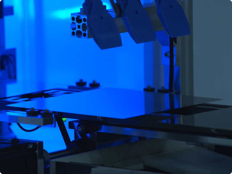 Close-up of a high-tech machine with mechanical arms holding a flat rectangular panel under blue lighting.