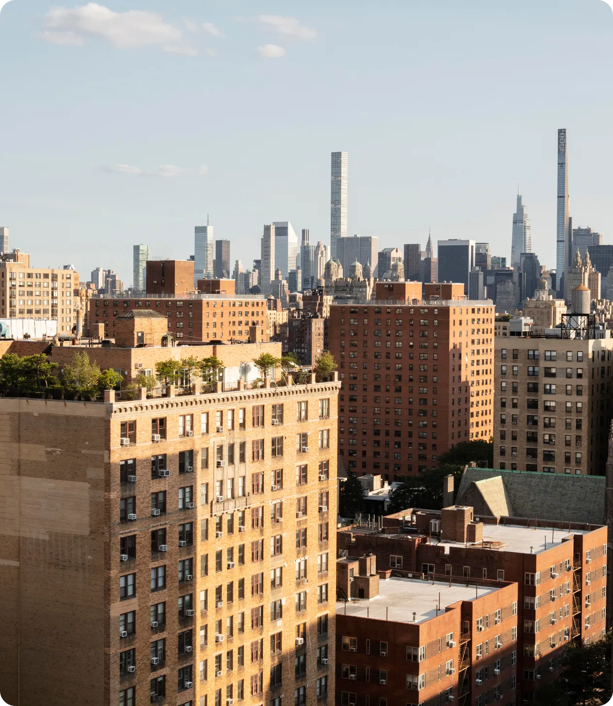 View of brick apartment buildings in foreground with New York City skyline in the background under a clear sky.