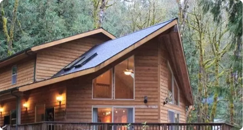 Wooden mountain cabin with large windows and warm interior lights surrounded by tall trees.