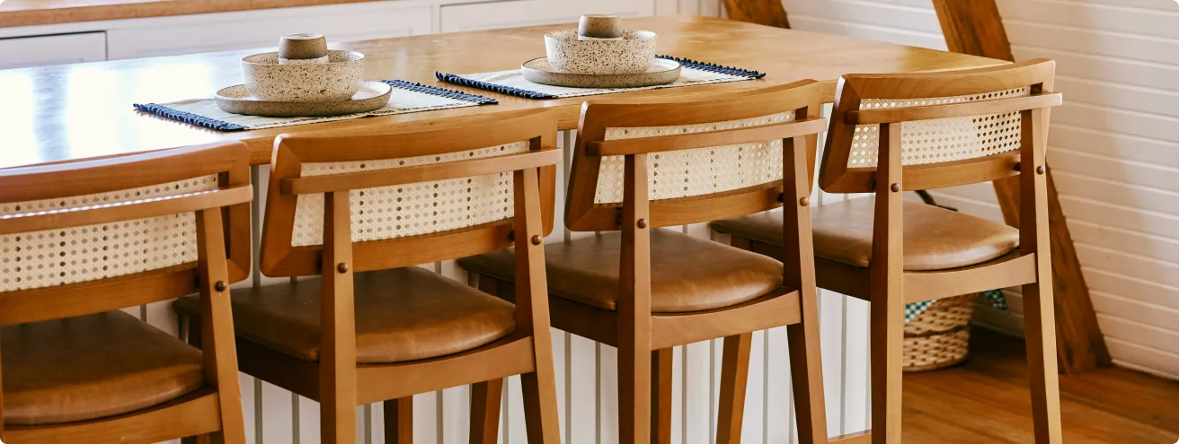 Wooden dining table with four matching chairs, each with woven cane backs and leather seat cushions, set with ceramic bowl and cup on woven placemats.