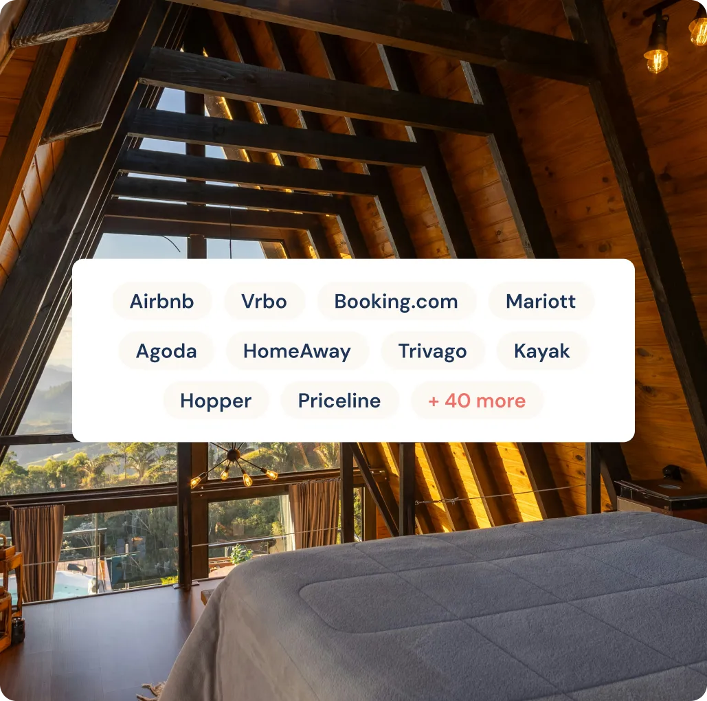 Interior view of a wooden A-frame cabin bedroom with large windows overlooking trees and hills at sunset.