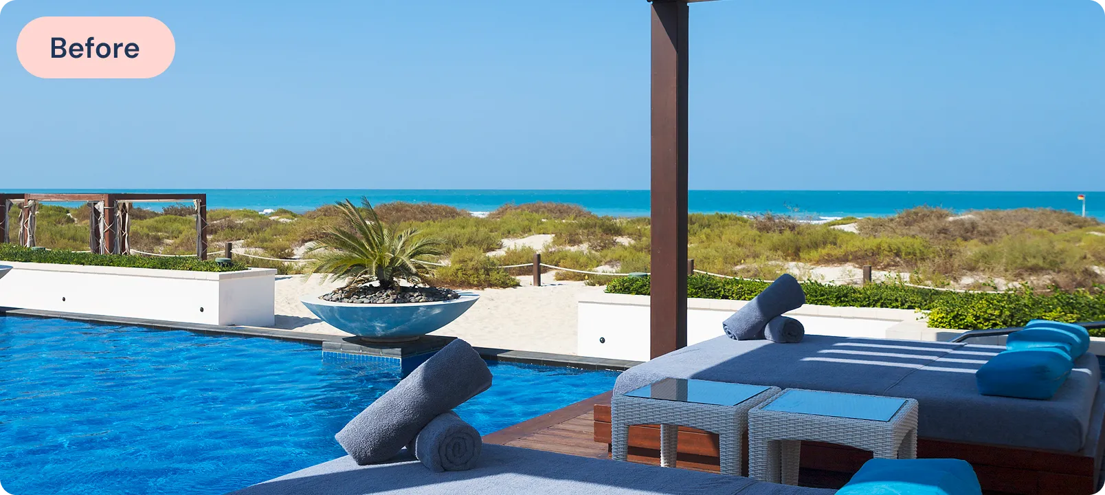 Poolside lounge beds with rolled towels and ocean view under clear blue sky.