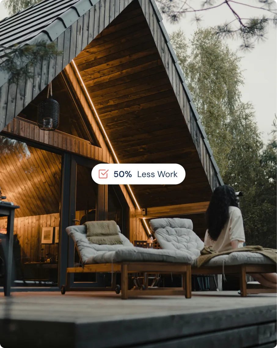 Modern wooden cabin with A-frame roof, two cushioned lounge chairs on the deck, and a woman sitting on one chair facing away.