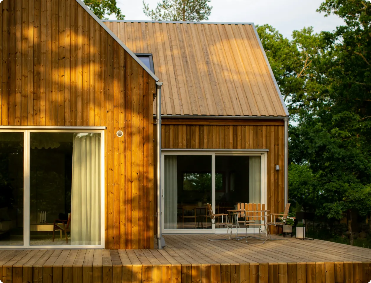 Modern wooden house with large sliding glass doors and a wooden deck with a table and chairs.