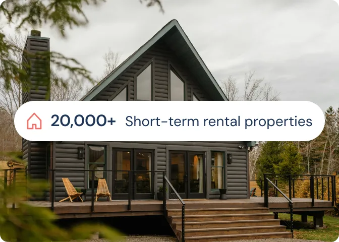 Modern large cabin-style house with a deck and wooden chairs, promoting over 20,000 short-term rental properties.