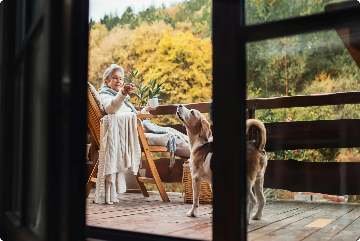 Elderly woman sitting on wooden deck with a dog looking up at her during autumn.