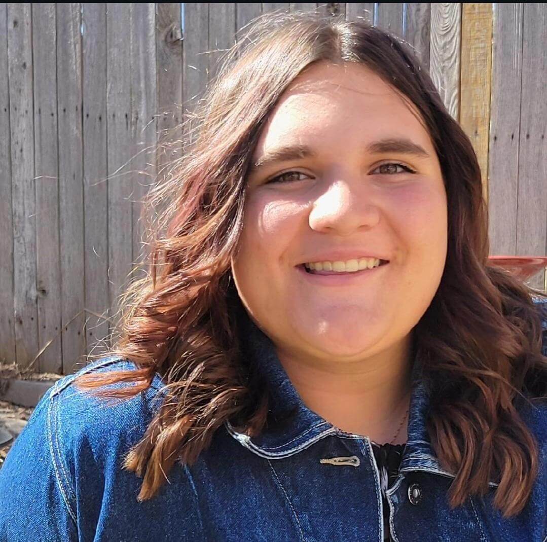 A photo of Robyn Foster, a staff member at Rock of Ages Lutheran Preschool and Childcare Center in Colorado Springs, CO. She is outside, smiling at the camera, with curled brown hair. 
