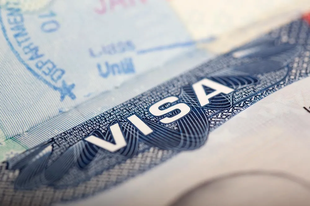 Primer plano de la palabra «VISA» en un visado estadounidense, con texto y sellos difuminados al fondo.