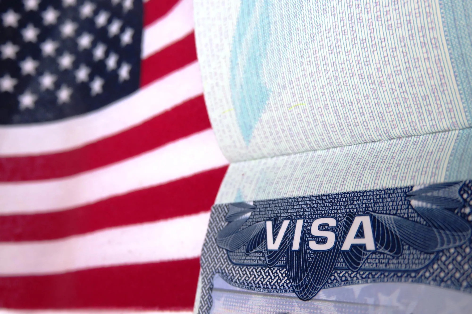 Primer plano de una página de pasaporte con visado estadounidense y bandera de EE. UU. difuminada al fondo.