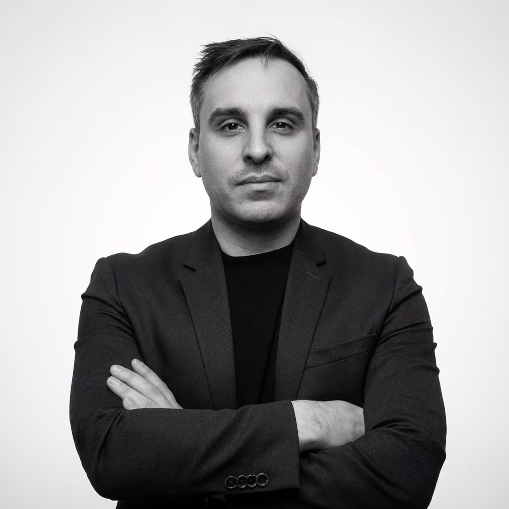 Portrait de Quentin : Homme aux cheveux courts, vêtu d'un blazer sombre et les bras croisés, regardant sérieusement vers l'avant.