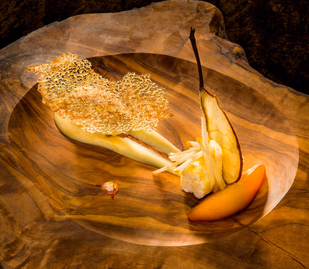 Dessert artistique avec poire tranchée, glace, chips croustillante dorée et pommes en julienne, présenté sur une assiette en bois sculpté.