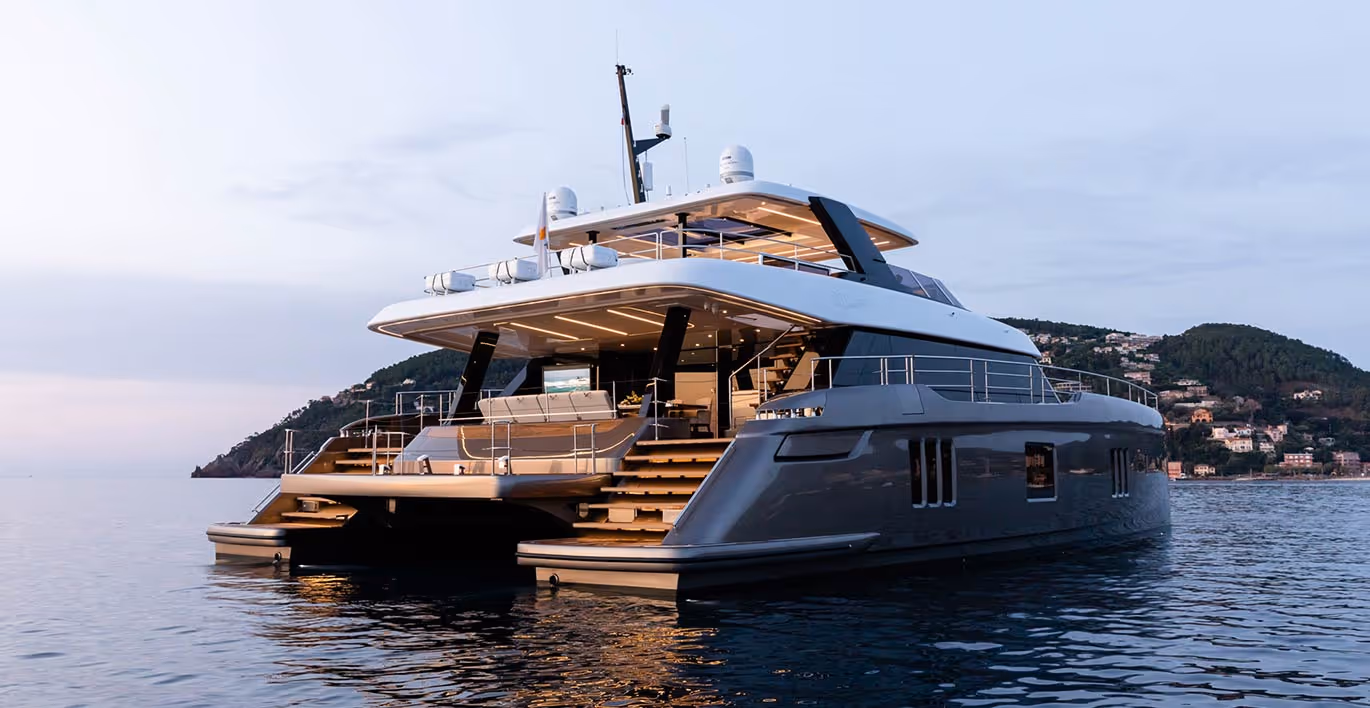 Vue arrière d'un grand yacht de luxe amarré sur une mer calme au coucher du soleil avec un paysage montagneux en arrière-plan.