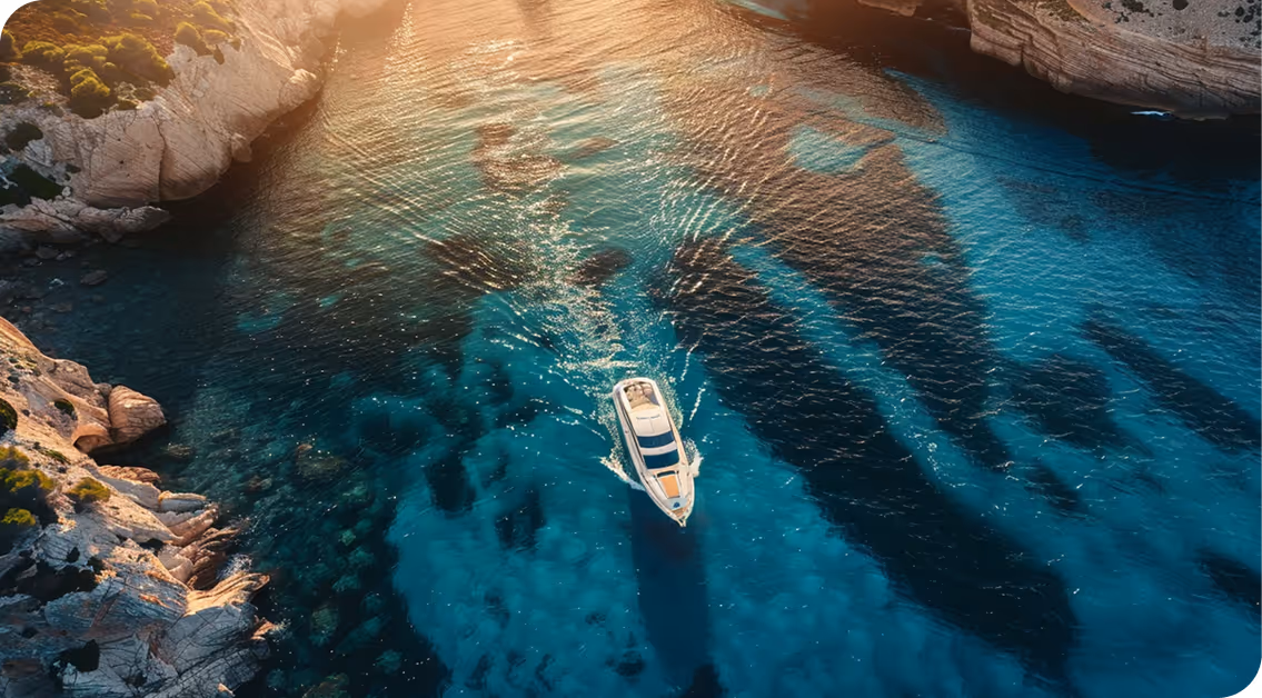 Bateau blanc naviguant sur une eau claire et turquoise entre des falaises rocheuses éclairées par un coucher de soleil.