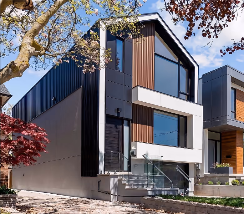 A modern two-story house with a gabled roof, featuring an exterior blend of black corrugated metal siding, white panels, vertical wood slat accents, large windows, and a glass-railed front staircase.   