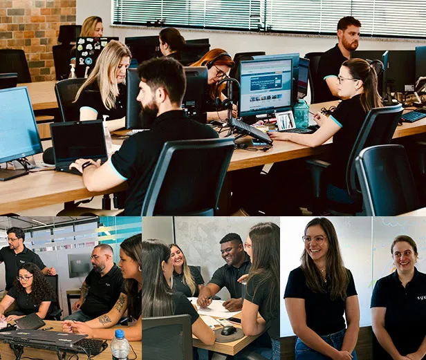 Equipe de escritório colaborando em mesas com computadores e reunião informal sorridente.
