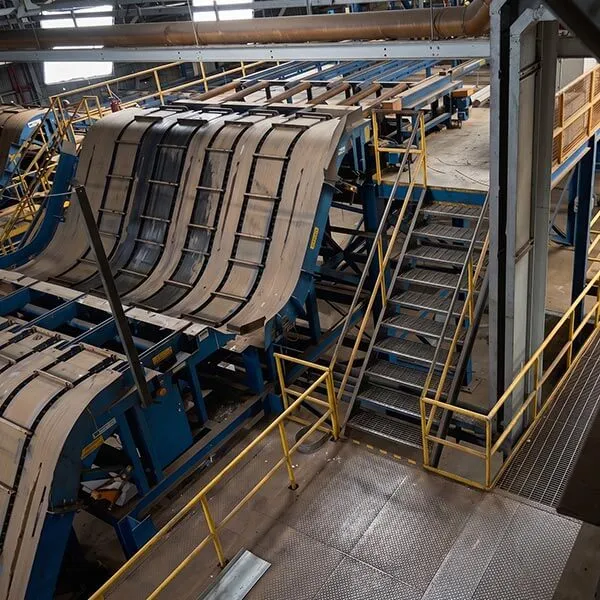 Esteira transportadora industrial azul e bege em fábrica com corrimãos amarelos e escada metálica.