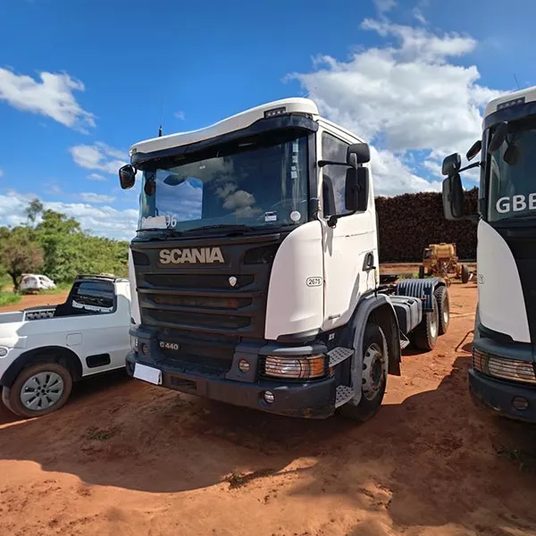 Caminhão Scania branco estacionado em área de terra sob céu azul com poucas nuvens.