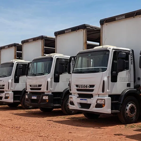 Fila de caminhões de carga Iveco brancos estacionados em terreno de terra sob céu azul.