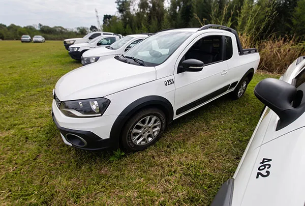 Caminhonete branca estacionada na grama com outras caminhonetes brancas alinhadas ao fundo.