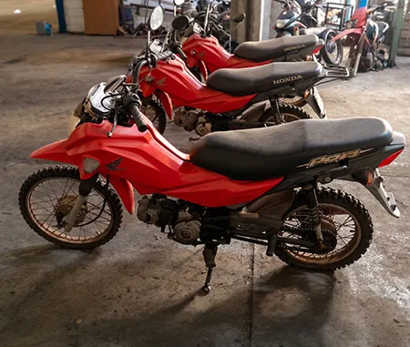 Duas motocicletas Honda Pop vermelhas estacionadas lado a lado em piso de concreto.