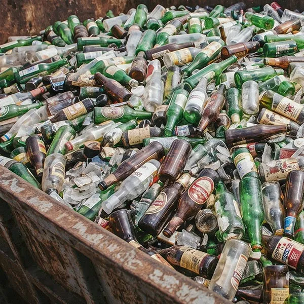 Caçamba cheia de garrafas de vidro verdes, marrons e transparentes para descarte.