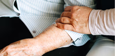 Hand hält unterstützend den Arm einer älteren Person.