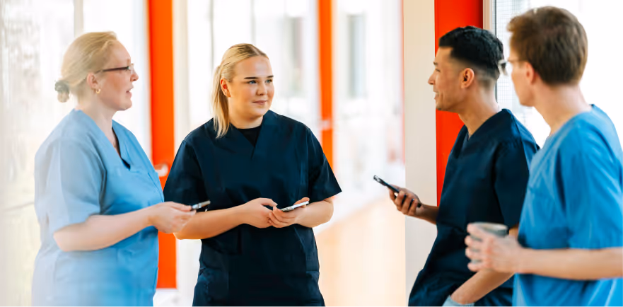 Vier medizinische Fachkräfte in Arbeitskleidung stehen im Flur und unterhalten sich.