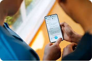 Zwei Personen sehen auf ein Smartphone mit Text auf dem Bildschirm, die eine hält das Gerät in der Hand.