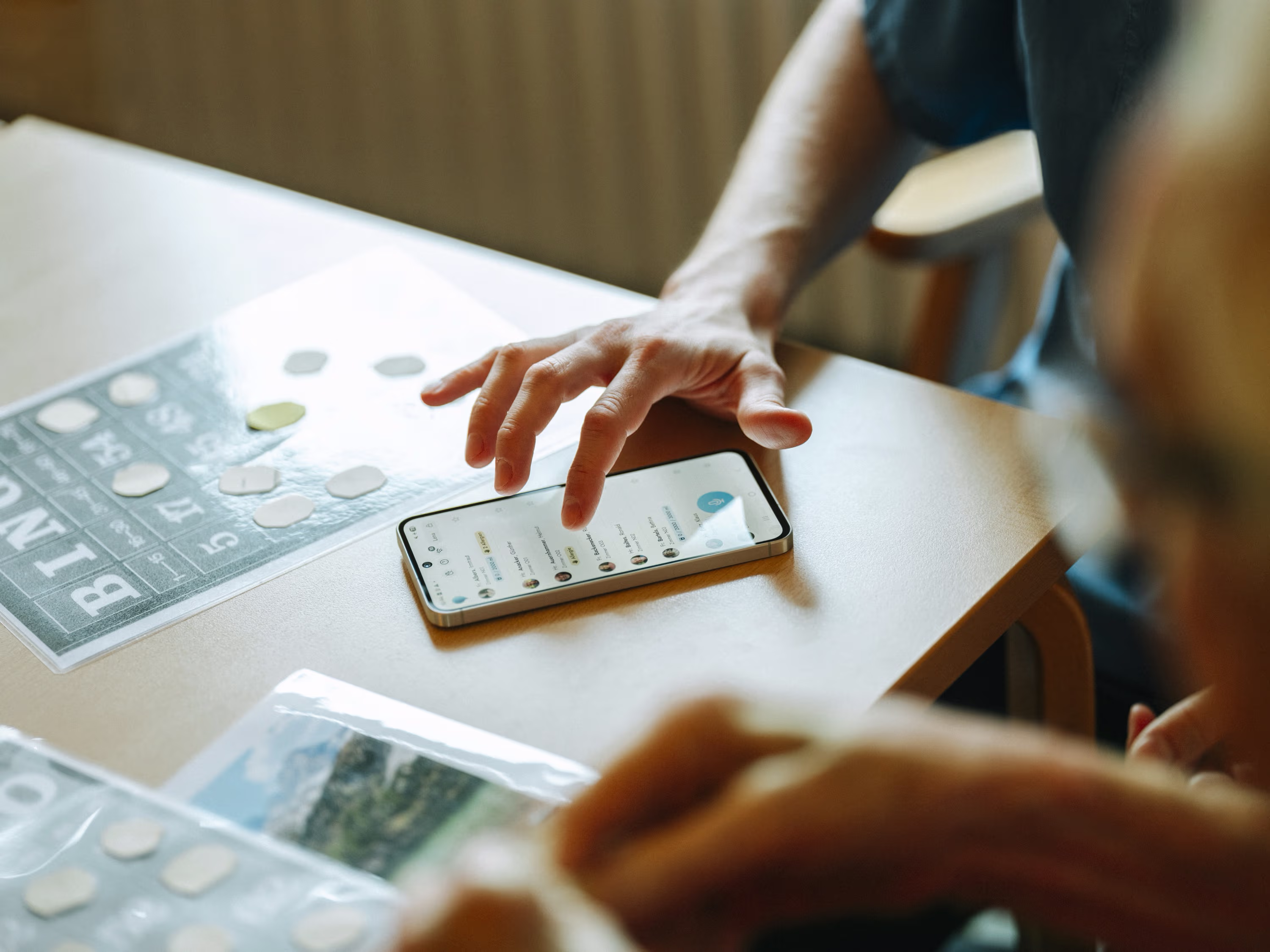 Hand tippt auf ein Smartphone mit Nachrichten-App neben einem Bingo-Spiel auf einem Tisch.