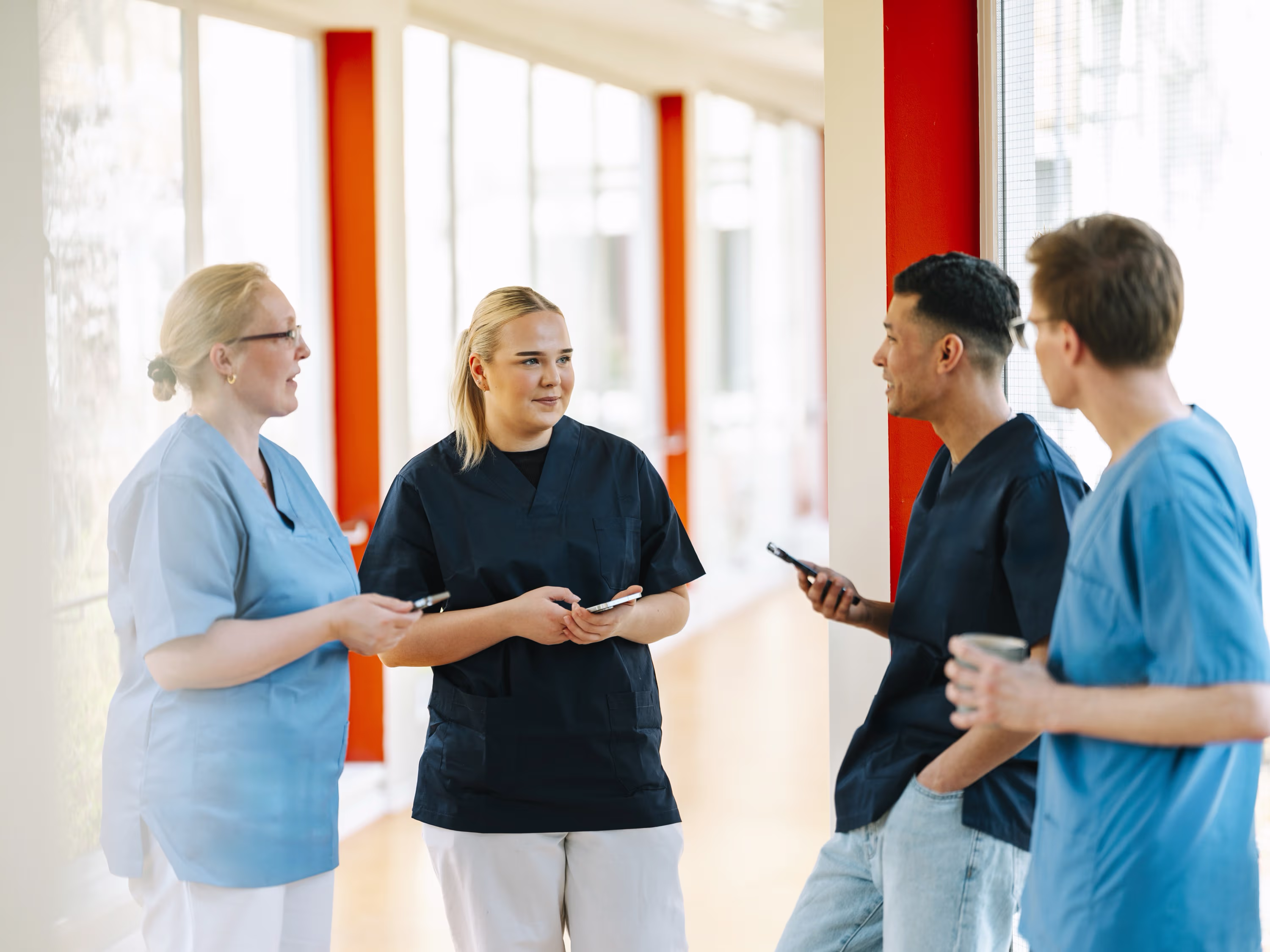 Vier medizinische Fachkräfte in Kitteln unterhalten sich im hellen Flur eines Krankenhauses.