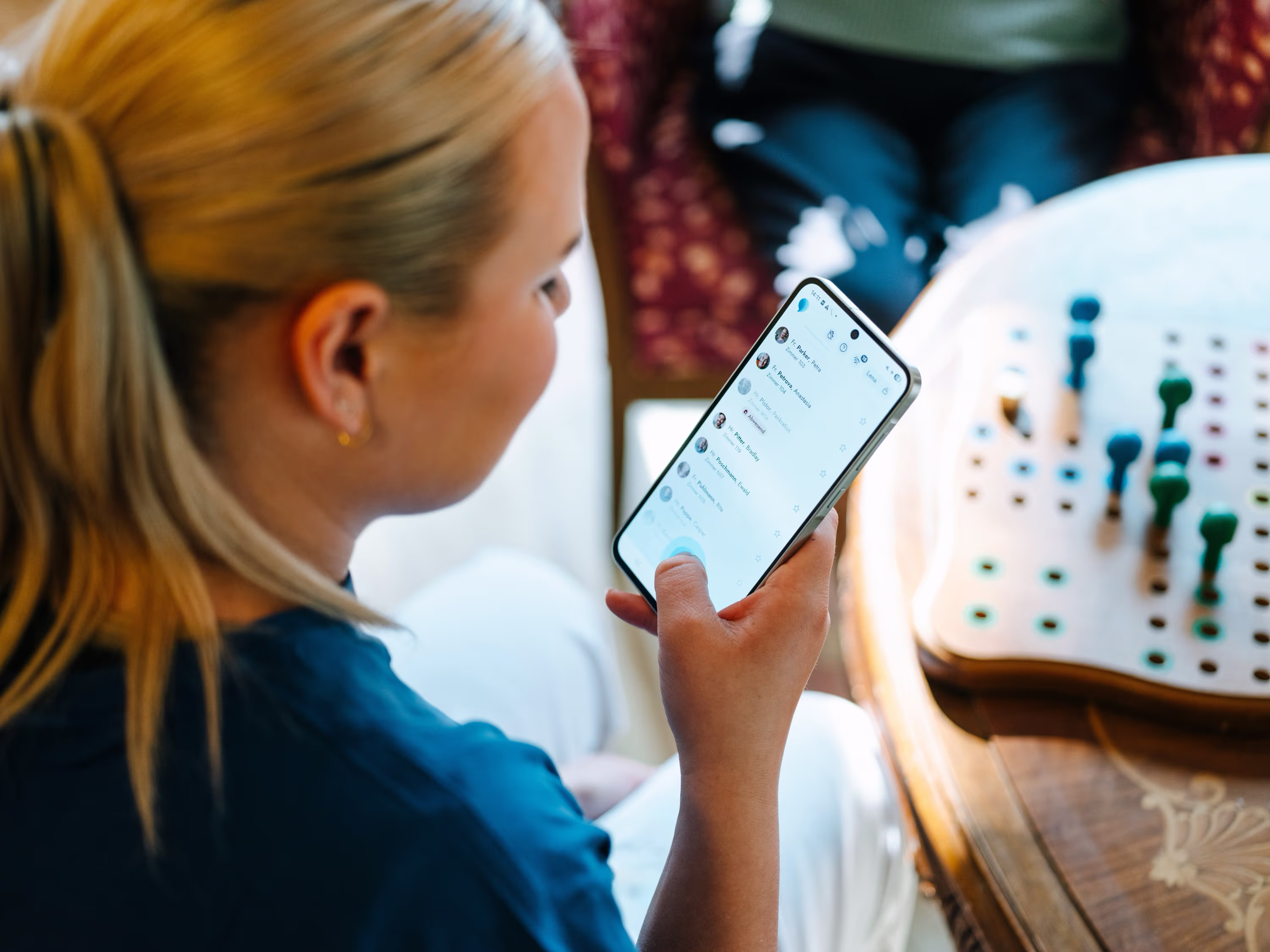 Frau mit blonden Haaren sieht sich eine Kontaktliste auf einem Smartphone an.