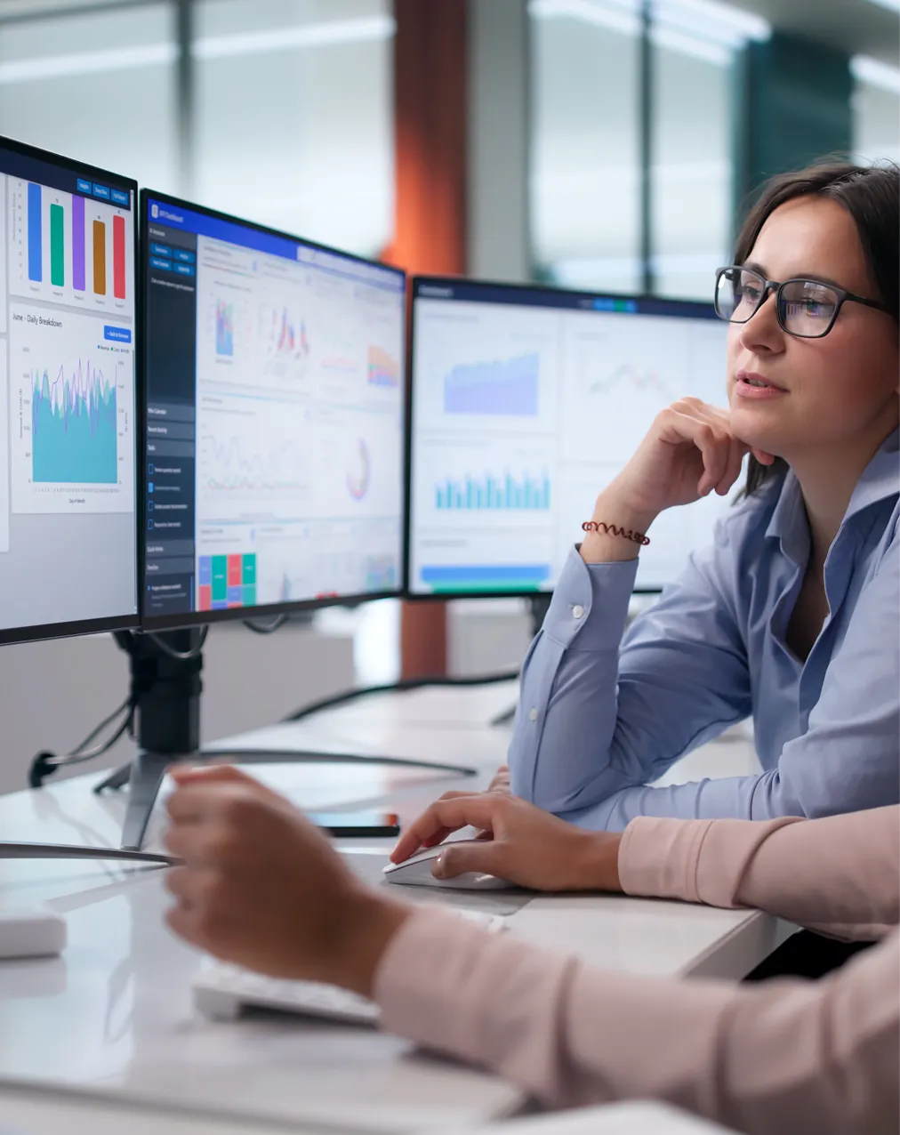 Two professionals analyzing data charts on three large computer monitors in an office.
