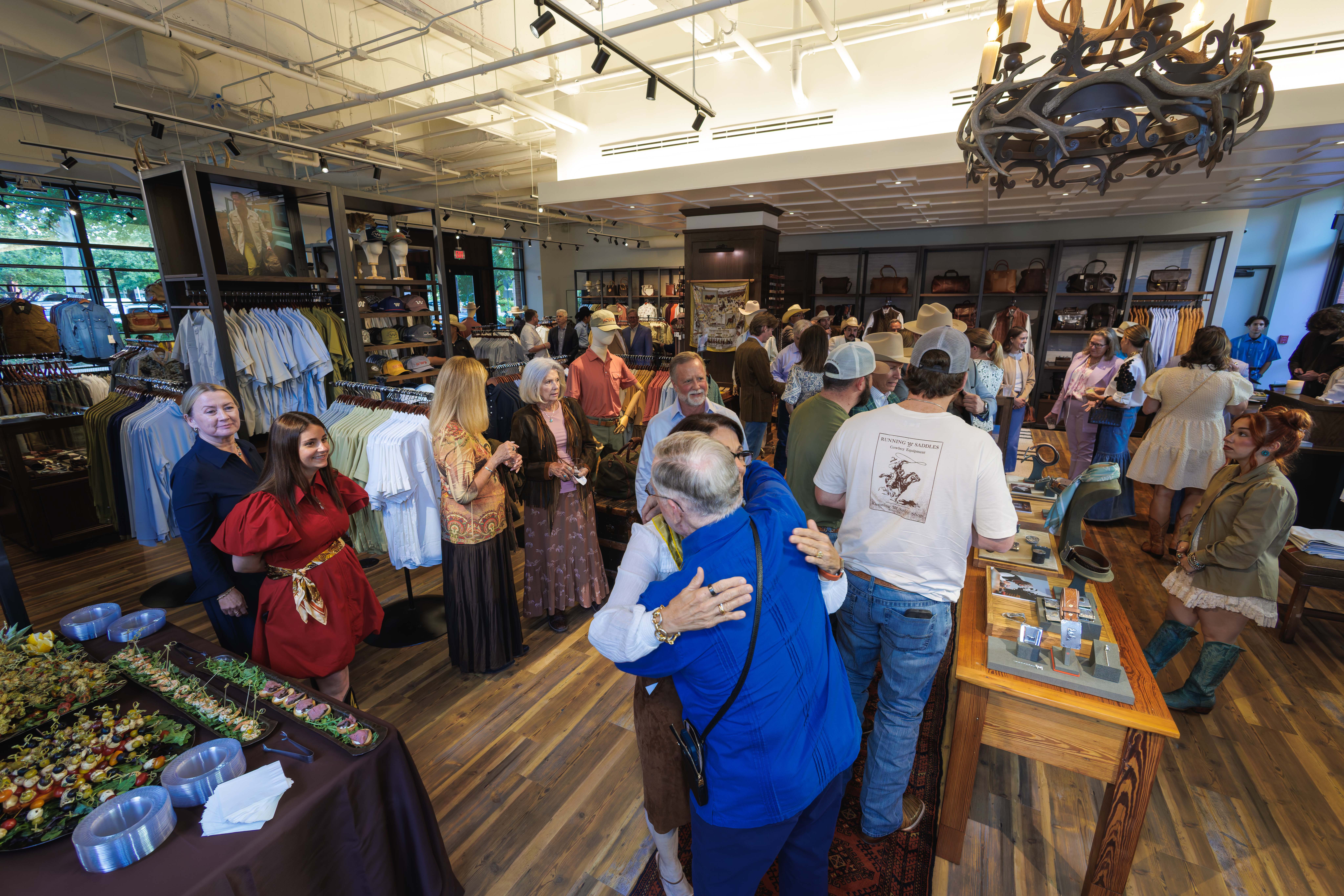 People socializing inside a clothing store with wooden floors, racks, and a table with small items.