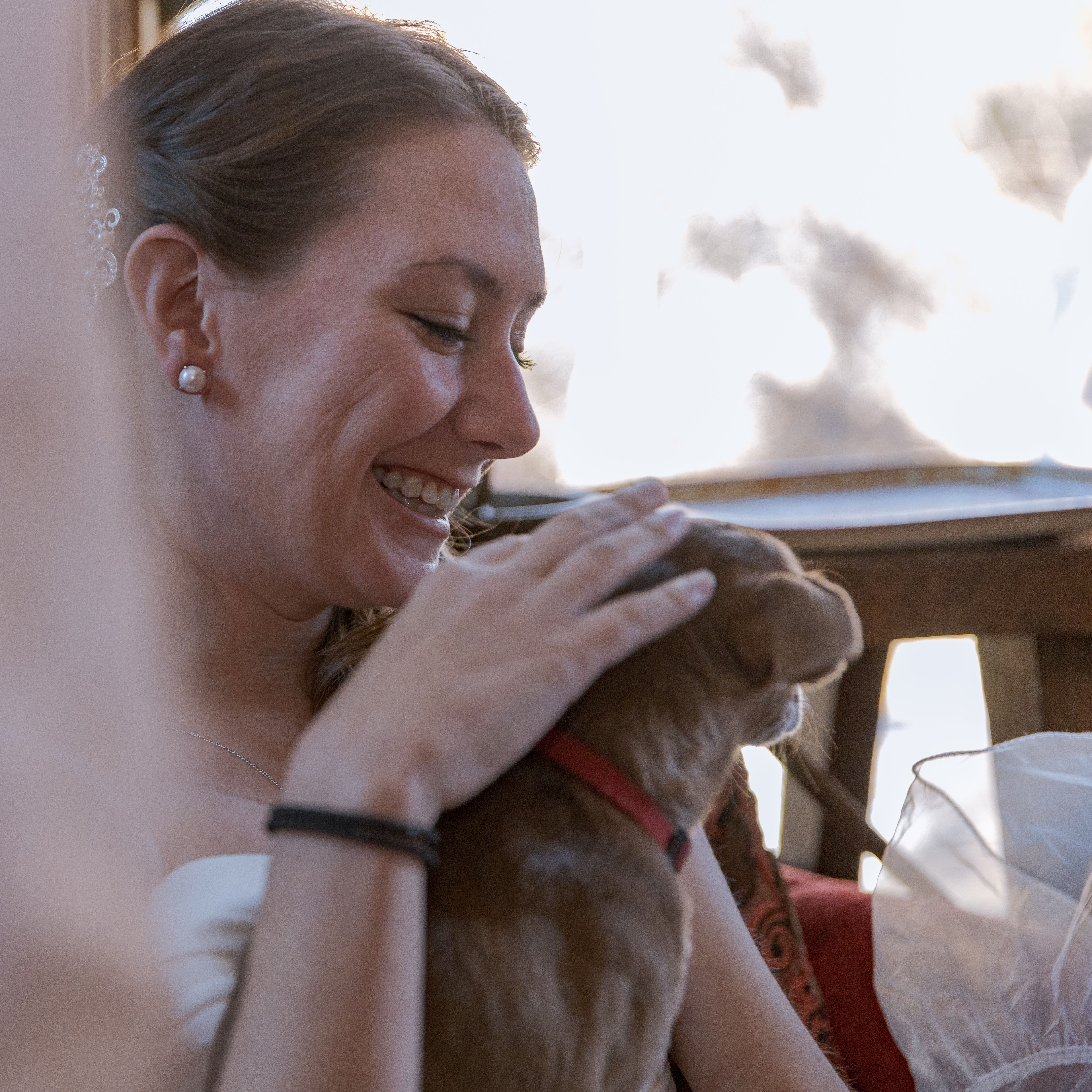 Smiling woman gently petting a small brown dog wearing a red collar indoors.