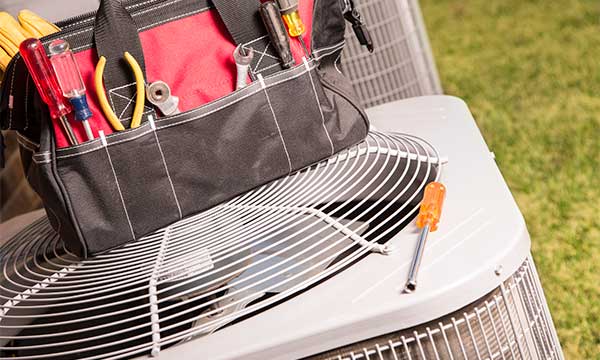 Black and red tool bag with various hand tools placed on top of a white outdoor air conditioning unit.