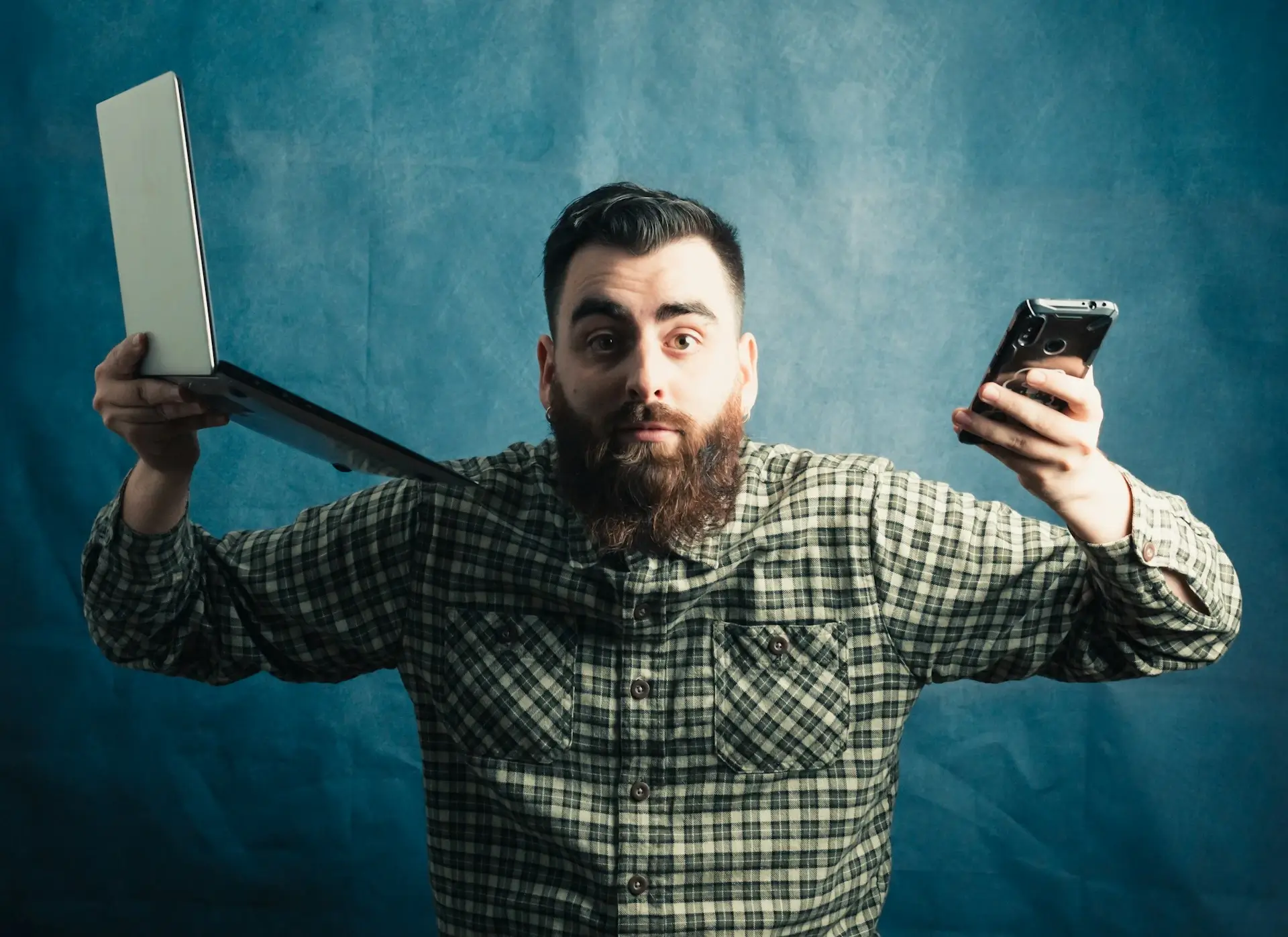 Niezdecydowany mężczyzna trzymający laptopa i telefon w rękach