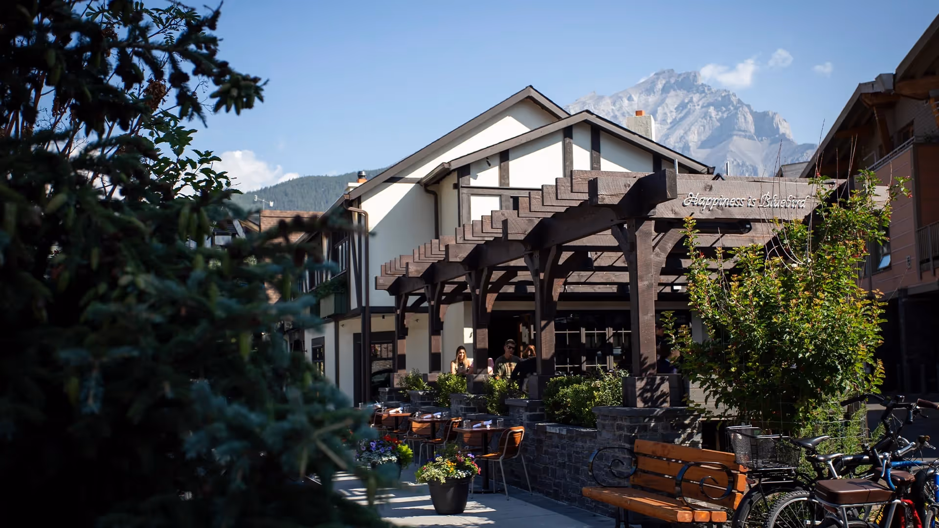 Outdoor seating area of a building with wooden pergola and mountain in the background.