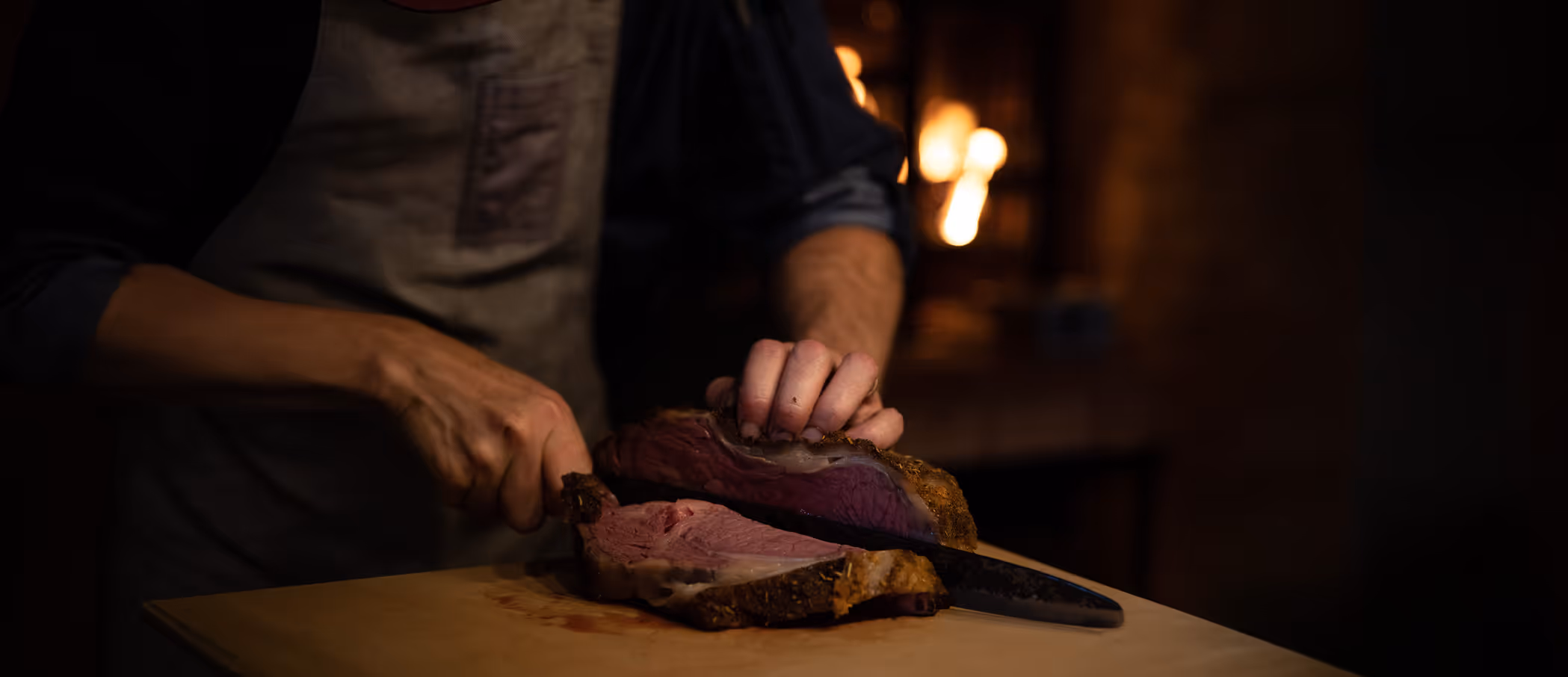 Person slicing a large piece of medium-rare roast beef on a wooden board.