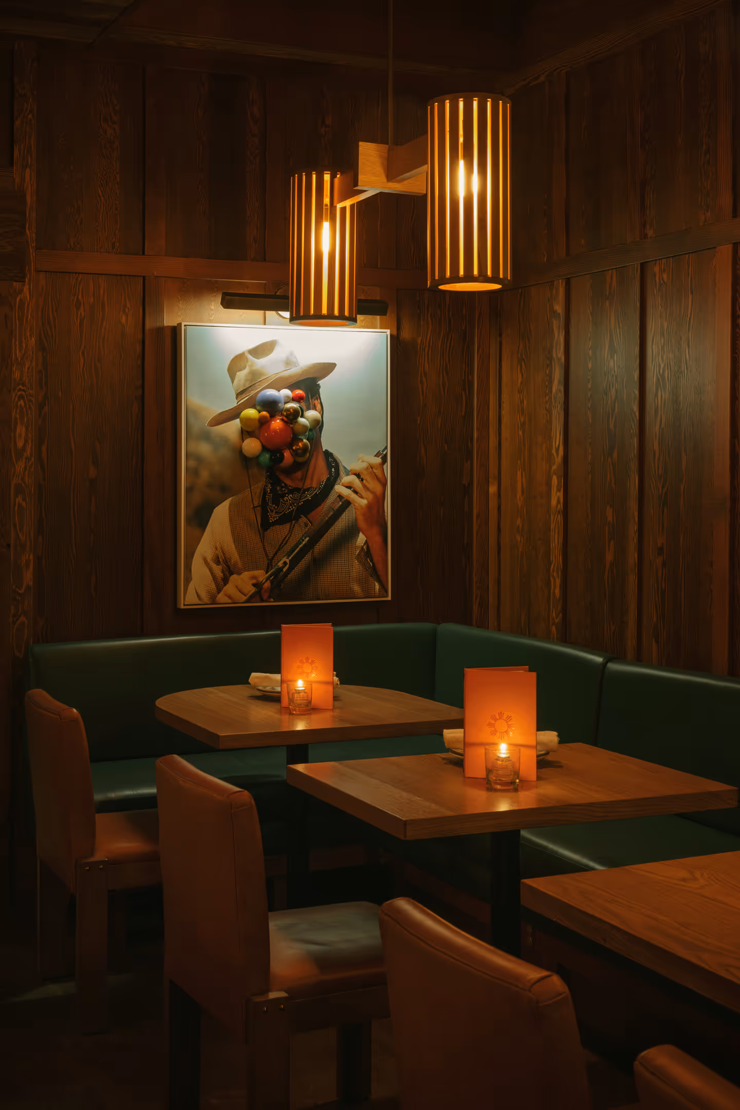 Cozy restaurant corner with wooden tables, green booth seating leather chairs, and warm pendant lights.