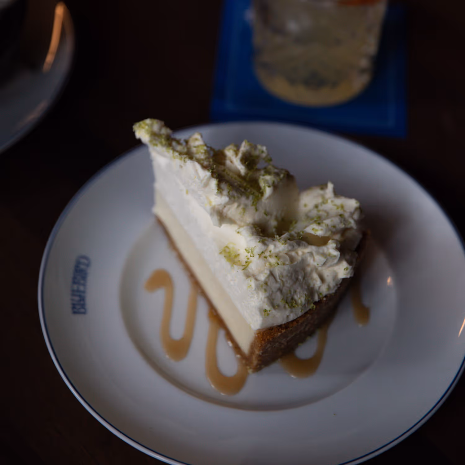 Slice of key lime pie with whipped cream and lime zest on a white plate with caramel sauce.