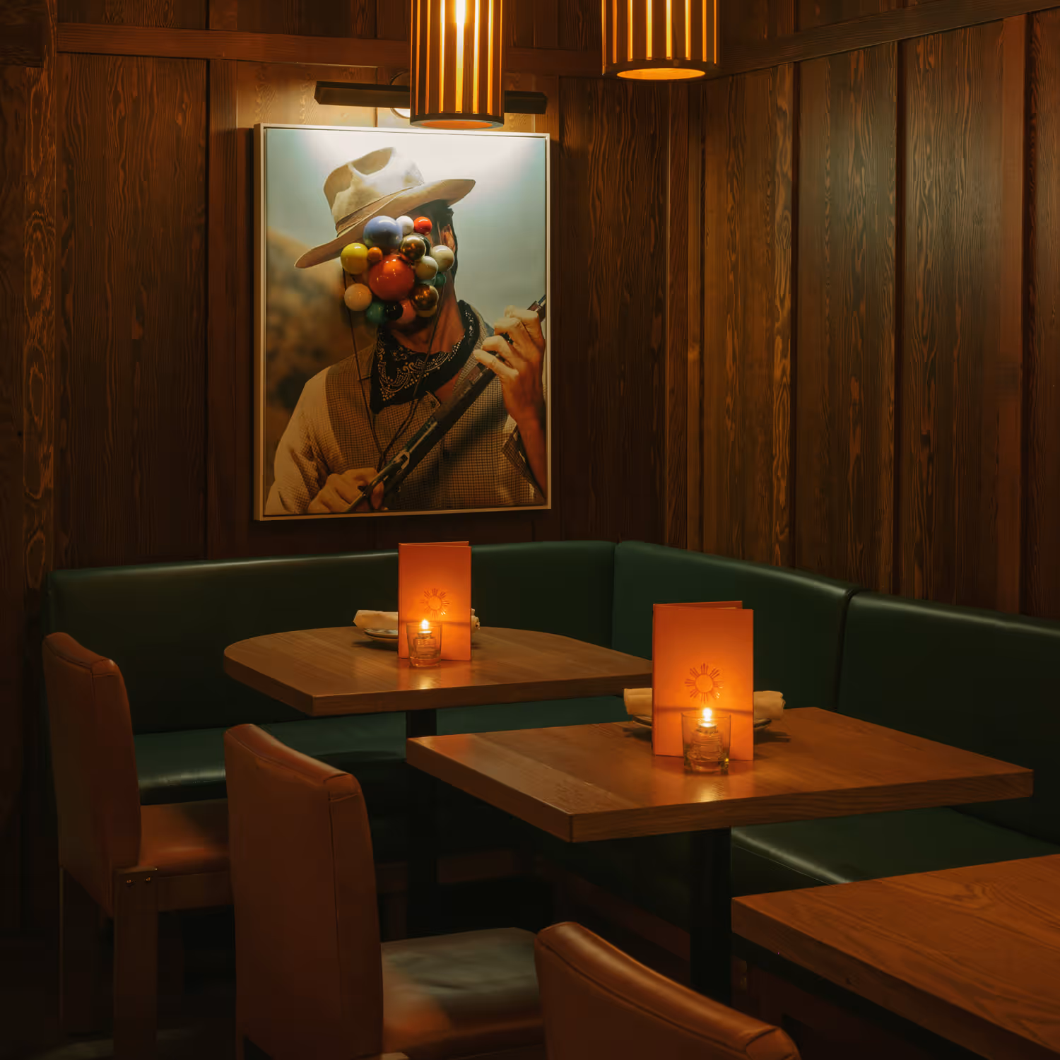 Cozy restaurant booth with green cushions, wooden tables, lit candles, and a framed artistic photo on wood-paneled walls.