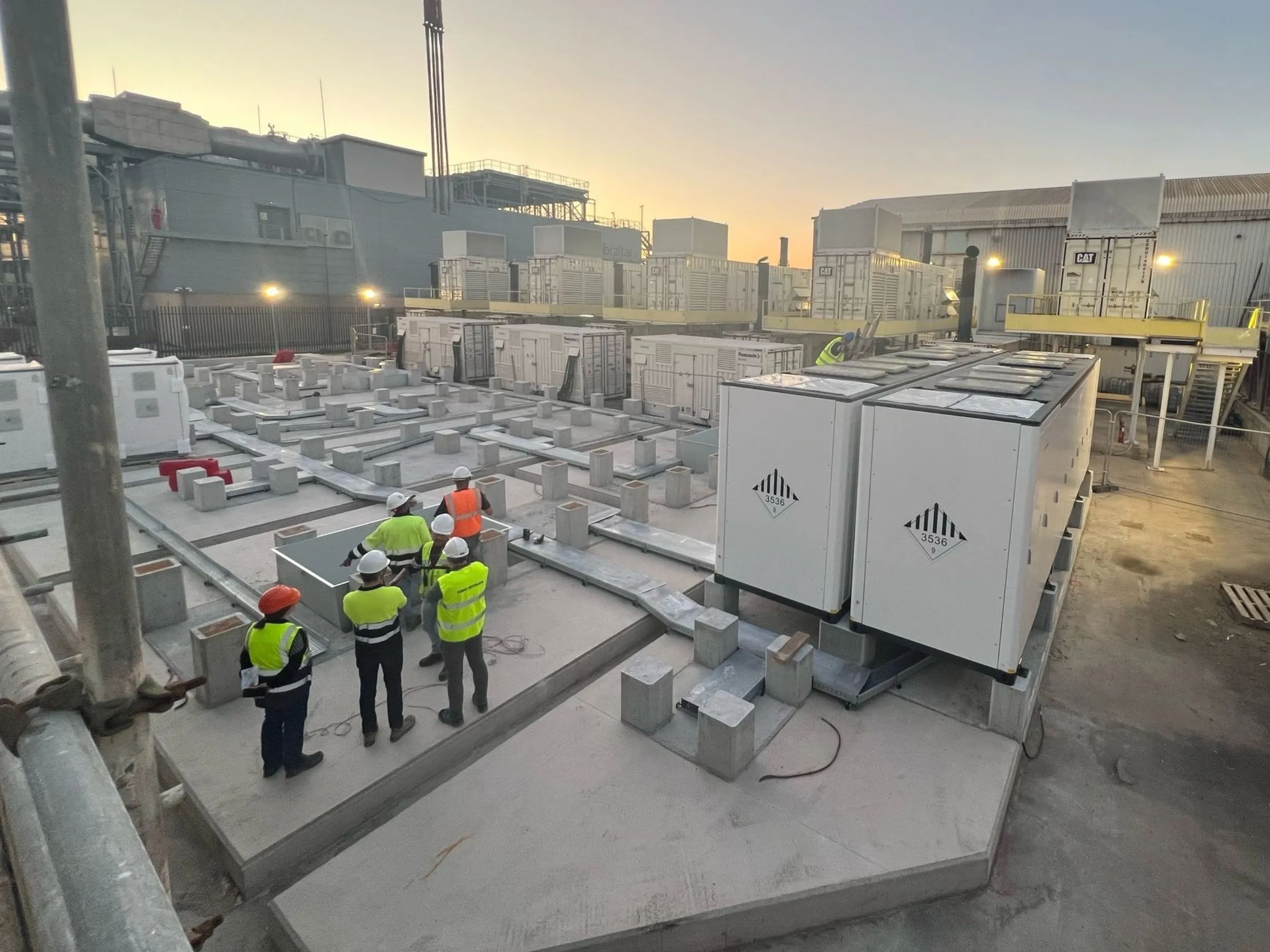Four workers inspecting battery energy storage units in industrial facility for renewables integration.