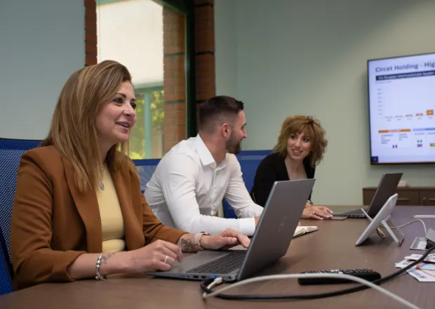 Three professionals collaborating at a conference table with laptops, discussing energy transition infrastructure projects.