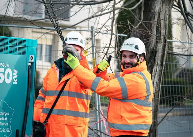 Two utility workers in high-visibility gear inspecting electric charging station for electric mobility infrastructure.