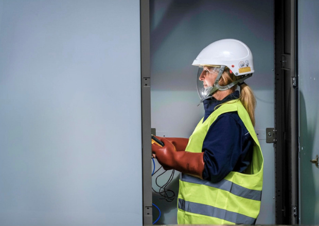 Technician inspecting high-voltage electrical infrastructure with safety gear and handheld device